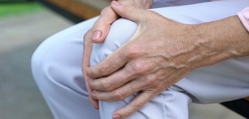 Vieille dame touchant son genou, assise sur un banc et prenant du tanezumab