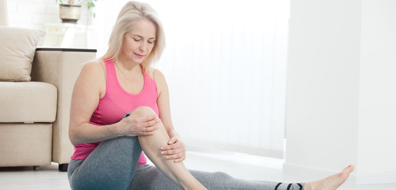 Femme assise par terre le genou pliée, les mains dessus